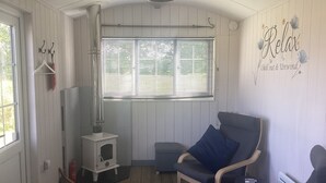 A cozy room with a wooden floor, a white heater, a blue chair, and a window with blinds. - Charming Luxurious Rural Shepherds Hut (Hook)