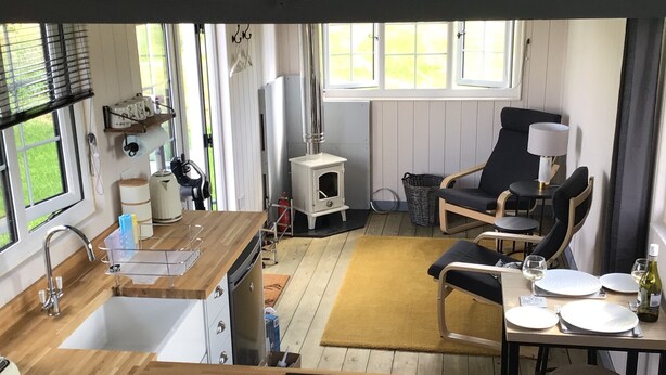 A compact kitchen with a built-in stove, a dining area with a table set for two, and a cozy seating area with a chair and a sofa. - Charming Luxurious Rural Shepherds Hut (Hook)