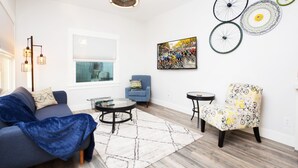 Una sala de estar moderna con sofá, sillón, mesa de centro y un adorno de rueda de bicicleta colgada en la pared.