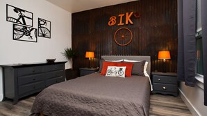 Un dormitorio moderno con una cama grande, dos mesitas de noche, un aparador y una obra de arte con bicicletas.