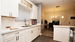 Una cocina moderna con armarios blancos, horno empotrado y comedor con mesa y sillas.