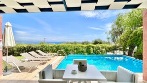 Ein Poolbereich mit Liegestühlen, einem Tisch und Blick auf das Meer.