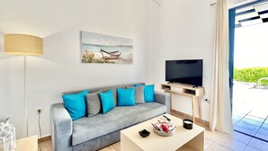 Ein modernes Wohnzimmer mit grauem Sofa, Couchtisch, Flachbildfernseher und einem Gemälde eines Bootes an der Wand.