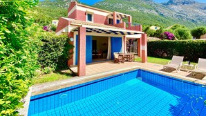 Ein zweistöckiges Gebäude mit Pool, umgeben von Grünflächen und Bergen.