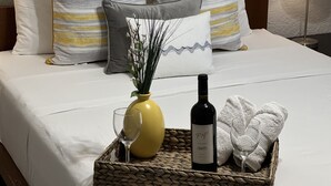 Ein ordentlich bezogenes Bett mit gestreiften Kissen, eine Vase mit Zweigen, eine Weinflasche und ein Korb mit Handtuch und Glas.
