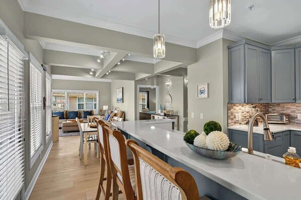 A modern kitchen with a large island, pendant lighting, and a view into the dining area.
