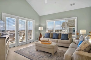 A living room with a sofa, ottoman, and a view through large windows.
