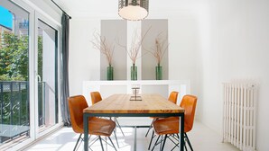Uma área de refeições com uma mesa de madeira, seis cadeiras de couro e três vasos verdes com galhos.