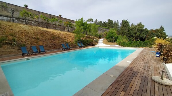 A swimming pool with blue water, surrounded by a wooden deck and a stone wall.