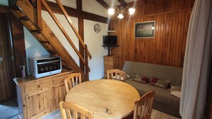 A cozy room with a wooden staircase, a dining table with chairs, a sofa, and a television on a wooden cabinet. - Chalet en Bois Dans Clairière à Pyrénées 2000 (Bolquère)