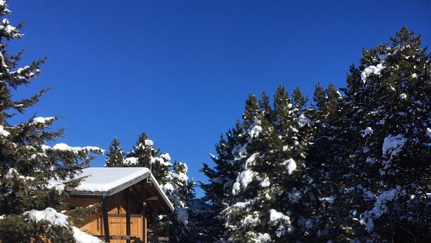 A wooden cabin with a snow-covered roof, surrounded by snow-laden trees and a wooden fence. - Chalet en Bois Dans Clairière à Pyrénées 2000 (Bolquère)