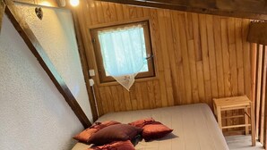 A wooden cabin room with a bed, pillows, a window, and a small table. - Chalet en Bois Dans Clairière à Pyrénées 2000 (Bolquère)