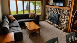 A cozy living room with a sectional sofa, a wooden coffee table, a stone fireplace, and a television. - Waterfront on Lake Huron- NEW Kitchen & Bathroom (Cheboygan)