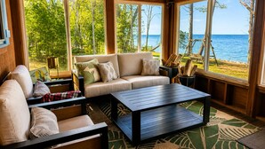 A cozy room with a sofa, a coffee table, and large windows offering a view of the beach and ocean. - Waterfront on Lake Huron- NEW Kitchen & Bathroom (Cheboygan)
