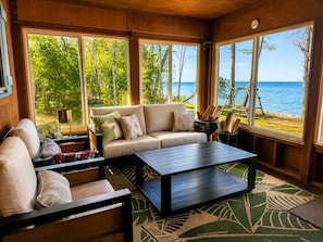 A cozy room with a sofa, a coffee table, and large windows offering a view of the beach and ocean.