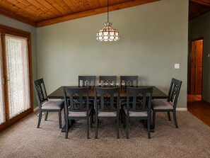 A dining room with a wooden table and chairs, a hanging light fixture, and a carpeted floor.