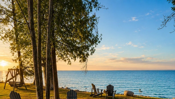 A lakeside outdoor seating area with Adirondack chairs, a fire pit, and a wooden bench. - Waterfront on Lake Huron- NEW Kitchen & Bathroom (Cheboygan)