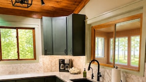 A kitchen with dark cabinets, a stainless steel dishwasher, a sink, and a window with a view of greenery. - Waterfront on Lake Huron- NEW Kitchen & Bathroom (Cheboygan)