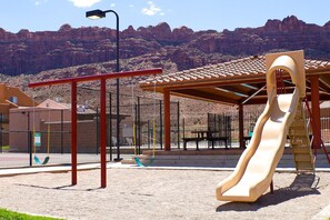 Kids can play on the playground's slide and swing set, while parents relax in the shaded seating area.