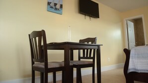 A dining area with a table and two chairs, a painting on the wall, and a television mounted above the table. - Private One Bedroom Cottage- Bonefish Creek (Barretarre)