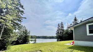 A house with a view of a lake, surrounded by trees and a well-maintained lawn. - Waterfront Cottage on Private Island near Acadia (Milbridge)