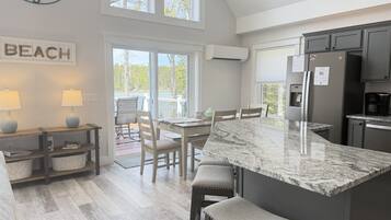 Une cuisine dotée d’un grand îlot central, un coin repas avec des chaises, une horloge et un panneau indiquant la mention « PLAGE ».