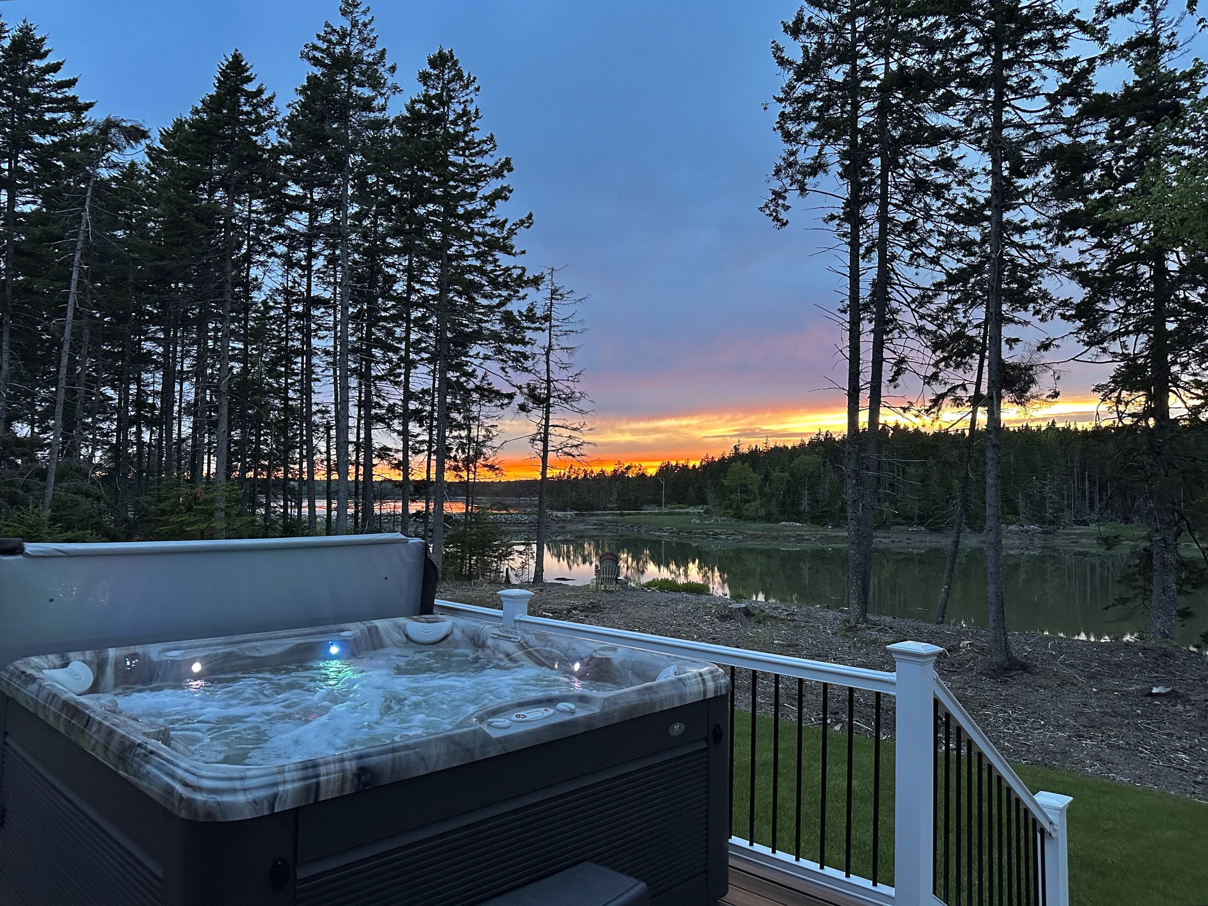 Ett bubbelbad på en terrass med utsikt över en sjö och en skog i solnedgången.