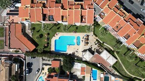 Vue aérienne d’un quartier résidentiel avec une grande piscine, plusieurs bâtiments aux toits recouverts de tuiles rouges et une végétation luxuriante tout autour.