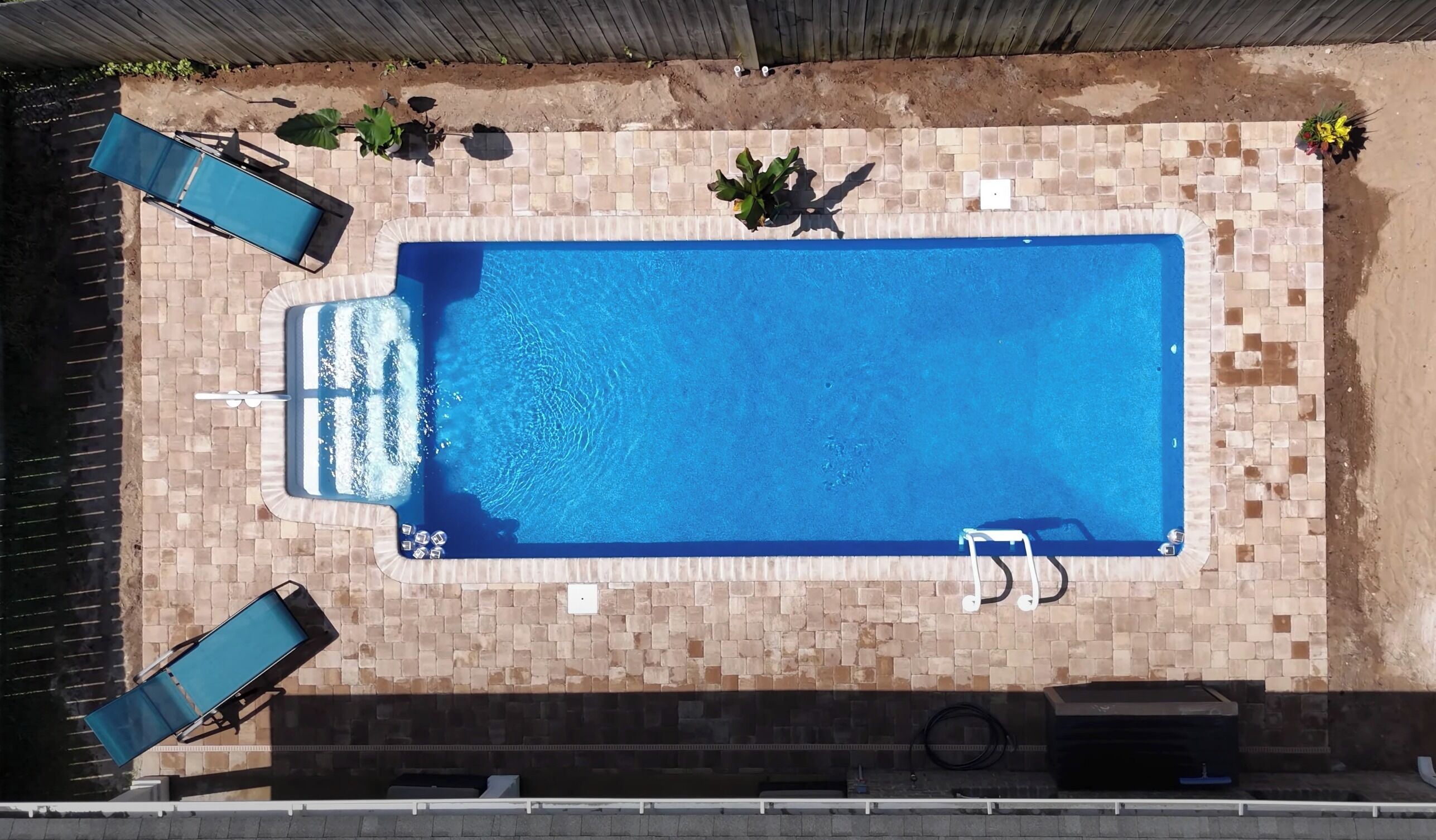 Una vista aerea di una piscina rettangolare con pareti piastrellate, circondata da un patio in mattoni.