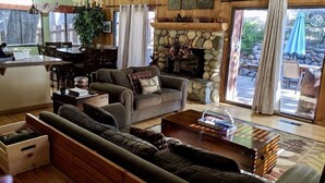 A cozy living room with a stone fireplace, a dining area with a wooden table and chairs, and a large window with curtains. - Quiet & Large house - Hot Tub, Pool table, Fast WiFi  -  close to Kings Beach! (Tahoe Vista)