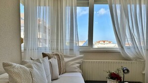 A living room with a sofa, a small table with a book and flowers, and sheer curtains. - Espacioso apartamento - El Nido de Ris 6918 (Noja)