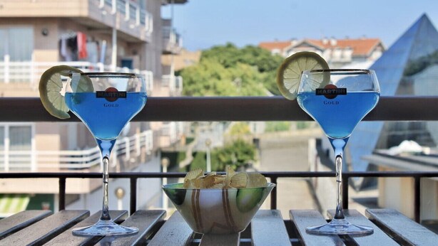 Two martini glasses with a blue cocktail on a balcony with a view of buildings and a pyramid in the background. - Espacioso apartamento - El Nido de Ris 6918 (Noja)