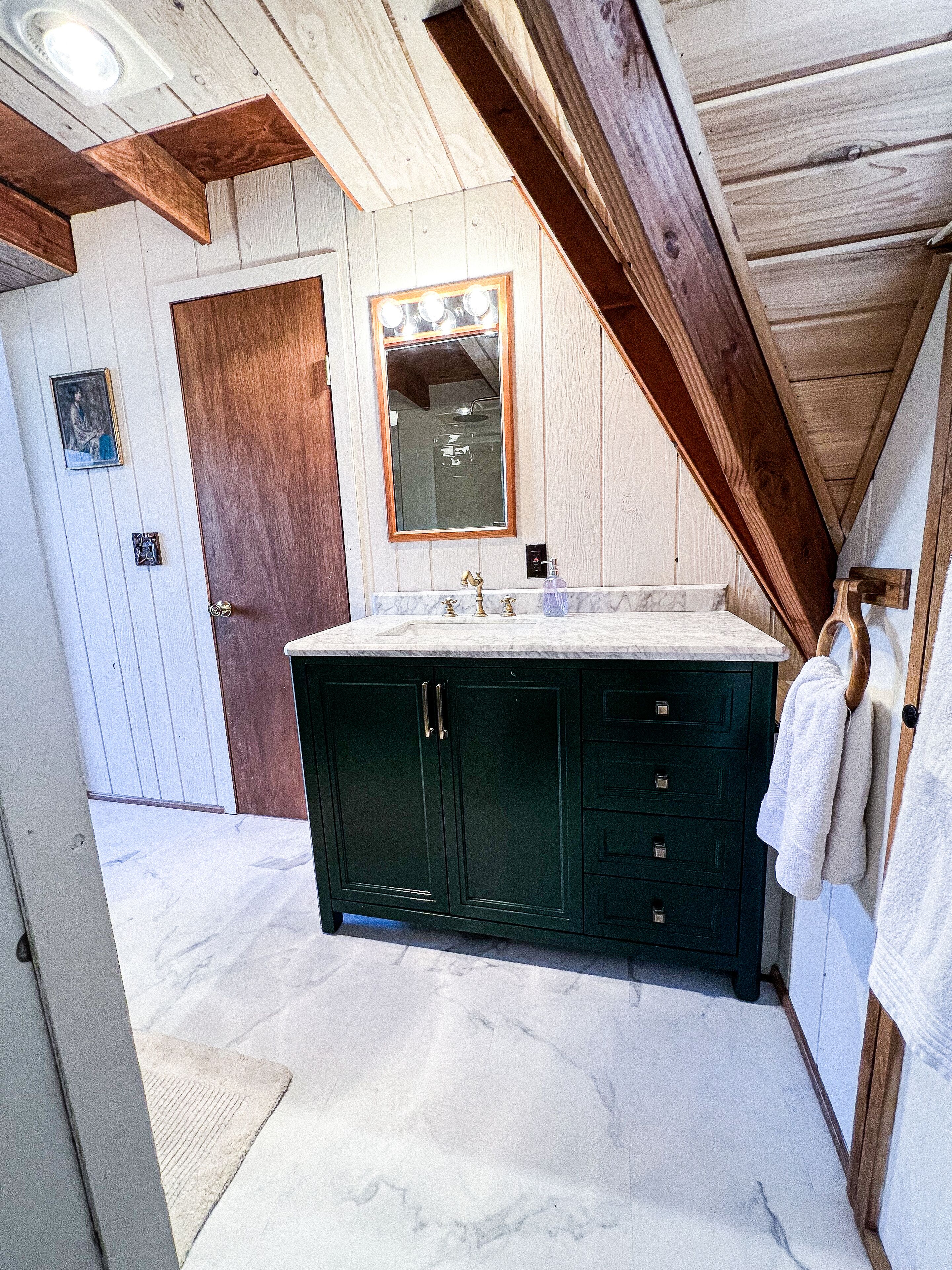 A bathroom with a large dark green vanity, a mirror above the sink, and a wooden ceiling.
