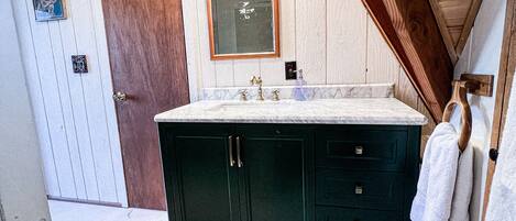 A bathroom with a large dark green vanity, a mirror above the sink, and a wooden ceiling.