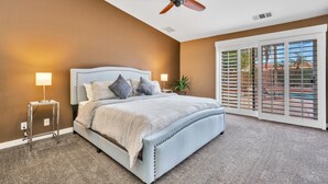 A bedroom with a bed, ceiling fan, bedside lamps, and a view through a sliding door. - Spacious Indio Oasis - Pool & Spa near Polo Ground (Indio)