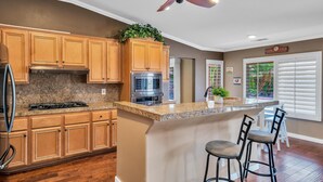 A kitchen with wooden cabinets, granite countertops, a stainless steel refrigerator, a built-in oven, and a ceiling fan. - Spacious Indio Oasis - Pool & Spa near Polo Ground (Indio)