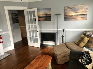A living room with a wooden coffee table, a sofa with a cushion, a guitar, a fireplace, and a painting on the wall. - The Apollo (Charleston)