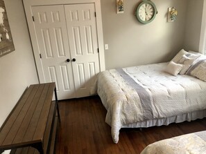 A bedroom with a wooden bench, a bed with a patterned bedspread, a wall clock, and a door. - The Apollo (Charleston)