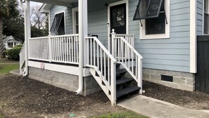 A house with a covered porch, a set of stairs leading to the front door, and a small front yard with mulch and grass. - The Apollo (Charleston)