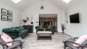 A spacious living room with two green sofas, a coffee table, and a TV mounted on the wall. - Ty Coch (Ruthin)