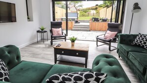 A modern living room with green sofas, a wooden coffee table, and two armchairs with cushions. - Ty Coch (Ruthin)