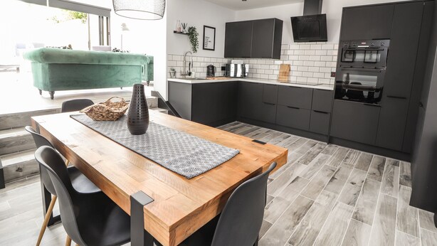A modern kitchen with dark cabinets, a wooden dining table, and a hanging light fixture. - Ty Coch (Ruthin)
