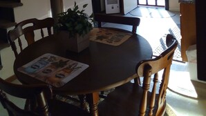 A dining area with a wooden table, chairs, and a chandelier. There is a refrigerator and a window in the background. - Reduced to 110.00 March-July  week nites (Weedville)