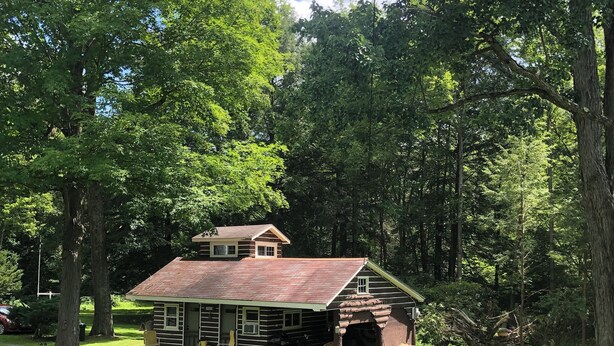 A rustic log cabin with a large porch and a chimney, surrounded by lush greenery and trees. - Reduced to 110.00 March-July  week nites (Weedville)