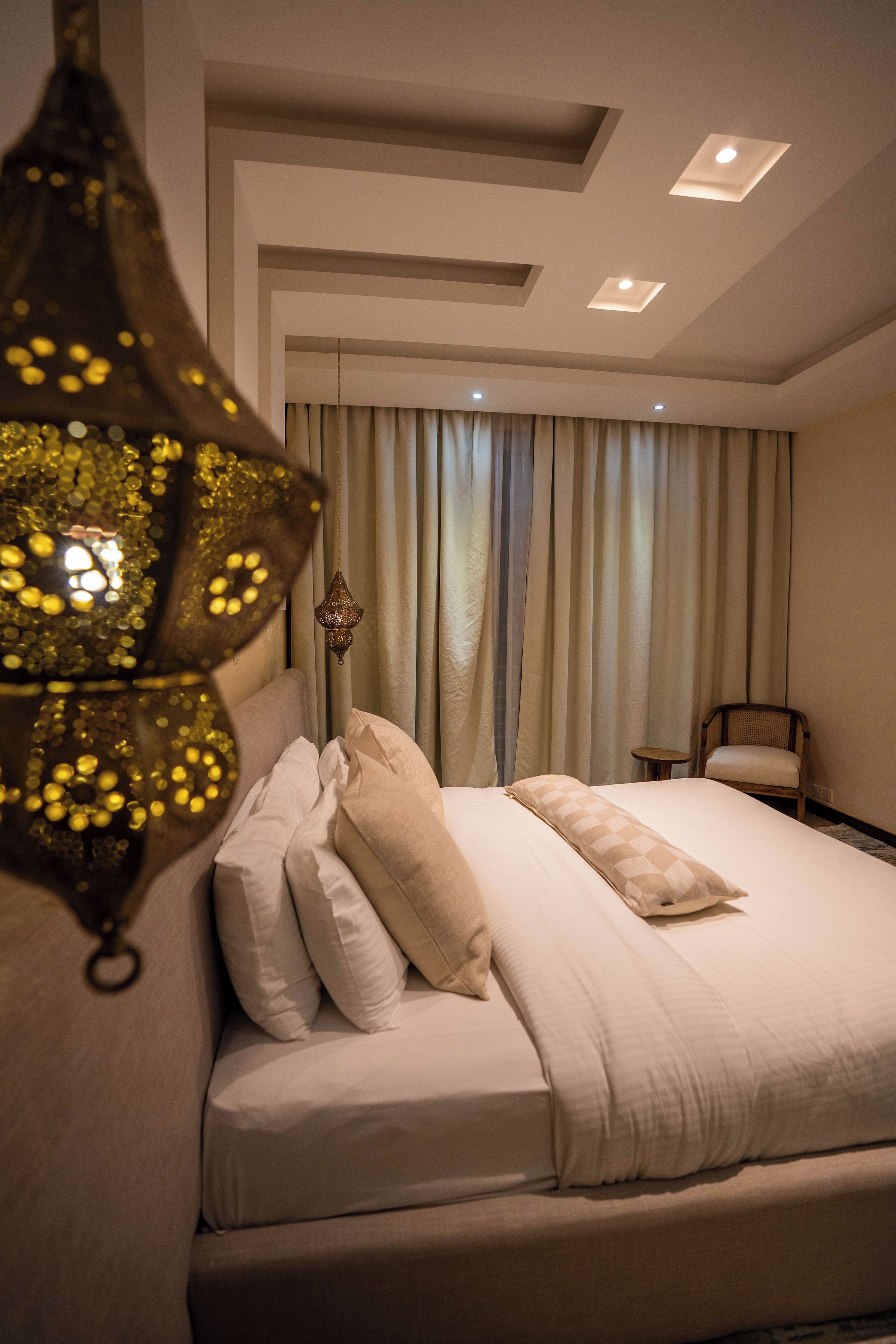 A hotel room with a bed, a hanging lamp, a chair, and a view of the outside through curtains.
