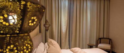 A hotel room with a bed, a hanging lamp, a chair, and a view of the outside through curtains.