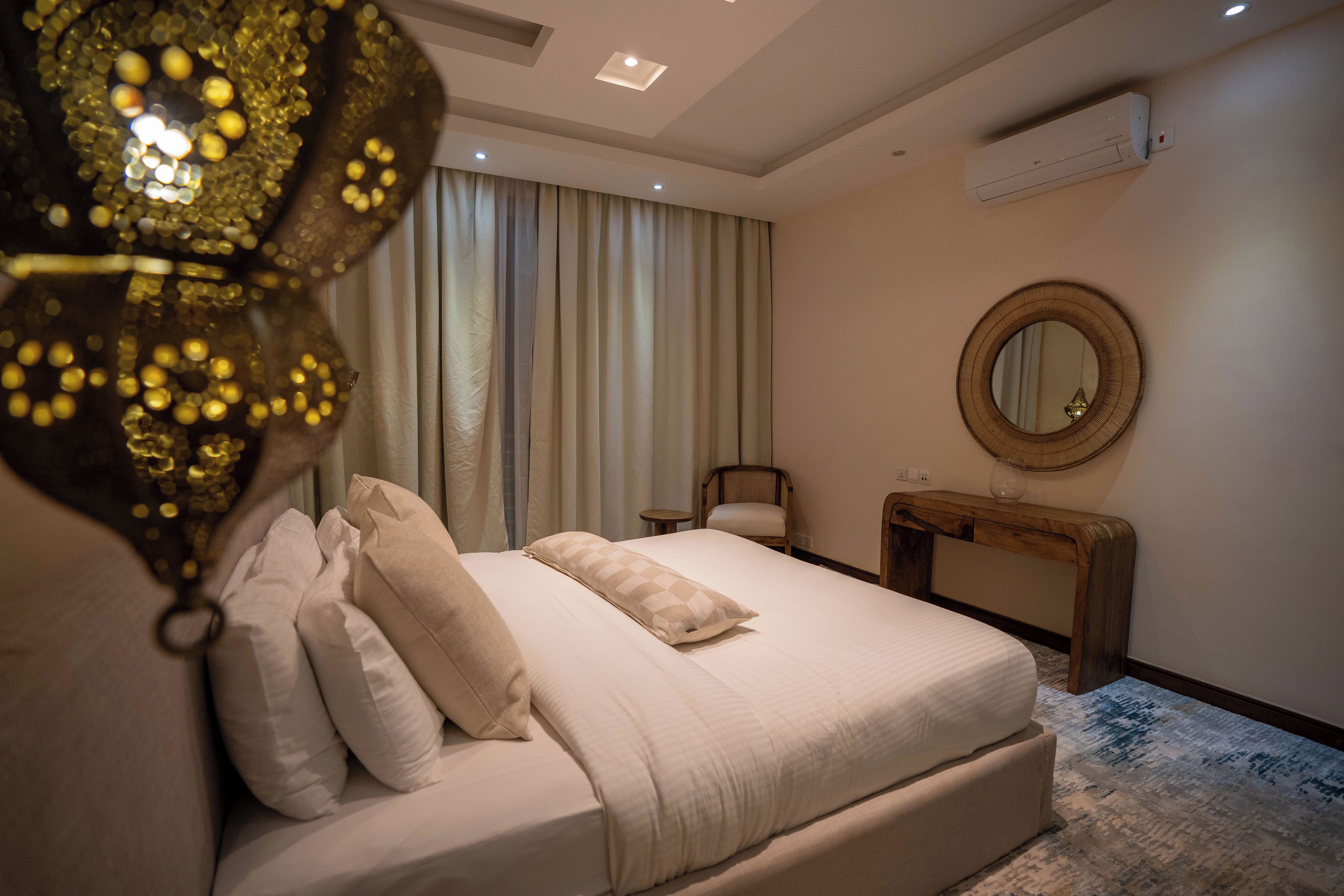 A modern bedroom with a large bed, a wooden nightstand, a round mirror, and a ceiling light fixture.