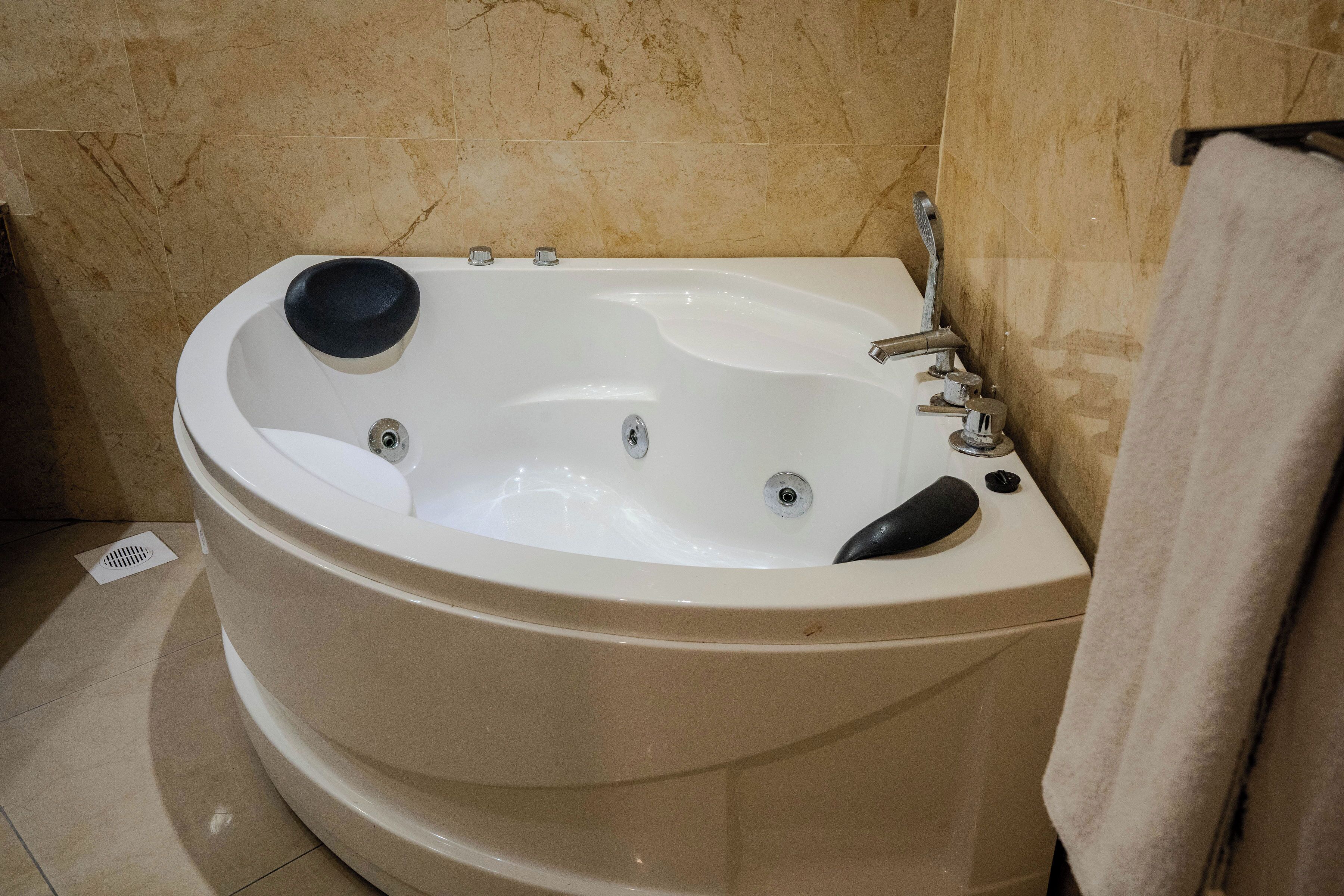 Une grande baignoire autoportante dotée d’un siège noir, d’une douchette et d’une serviette accrochée au mur.