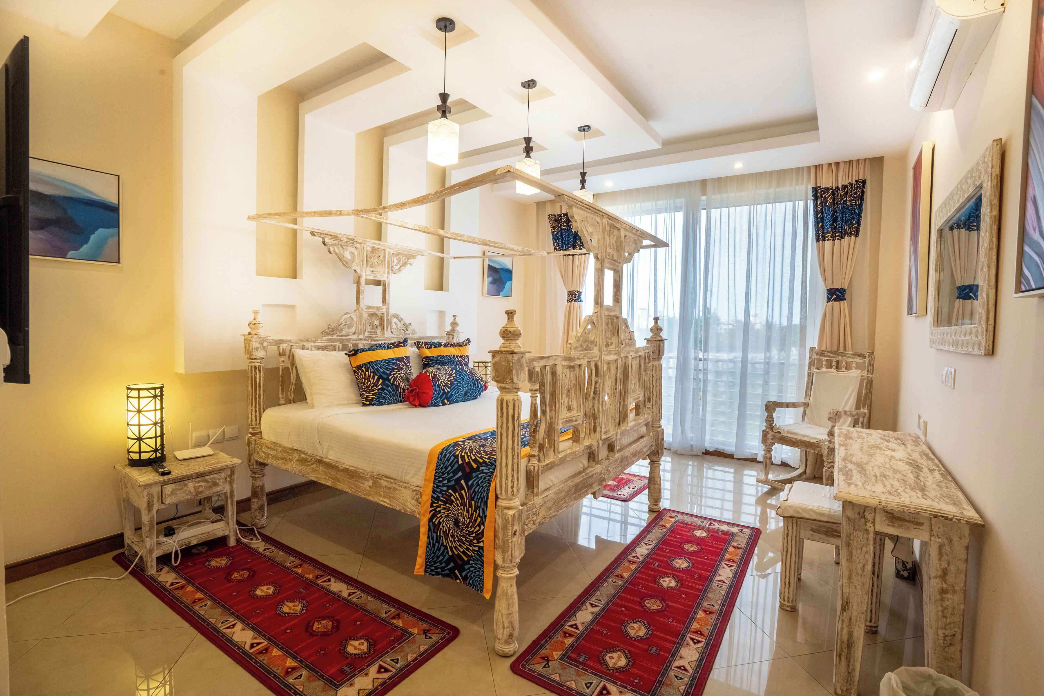 A bedroom with a four-poster bed, a small table, a chair, and a red patterned rug.