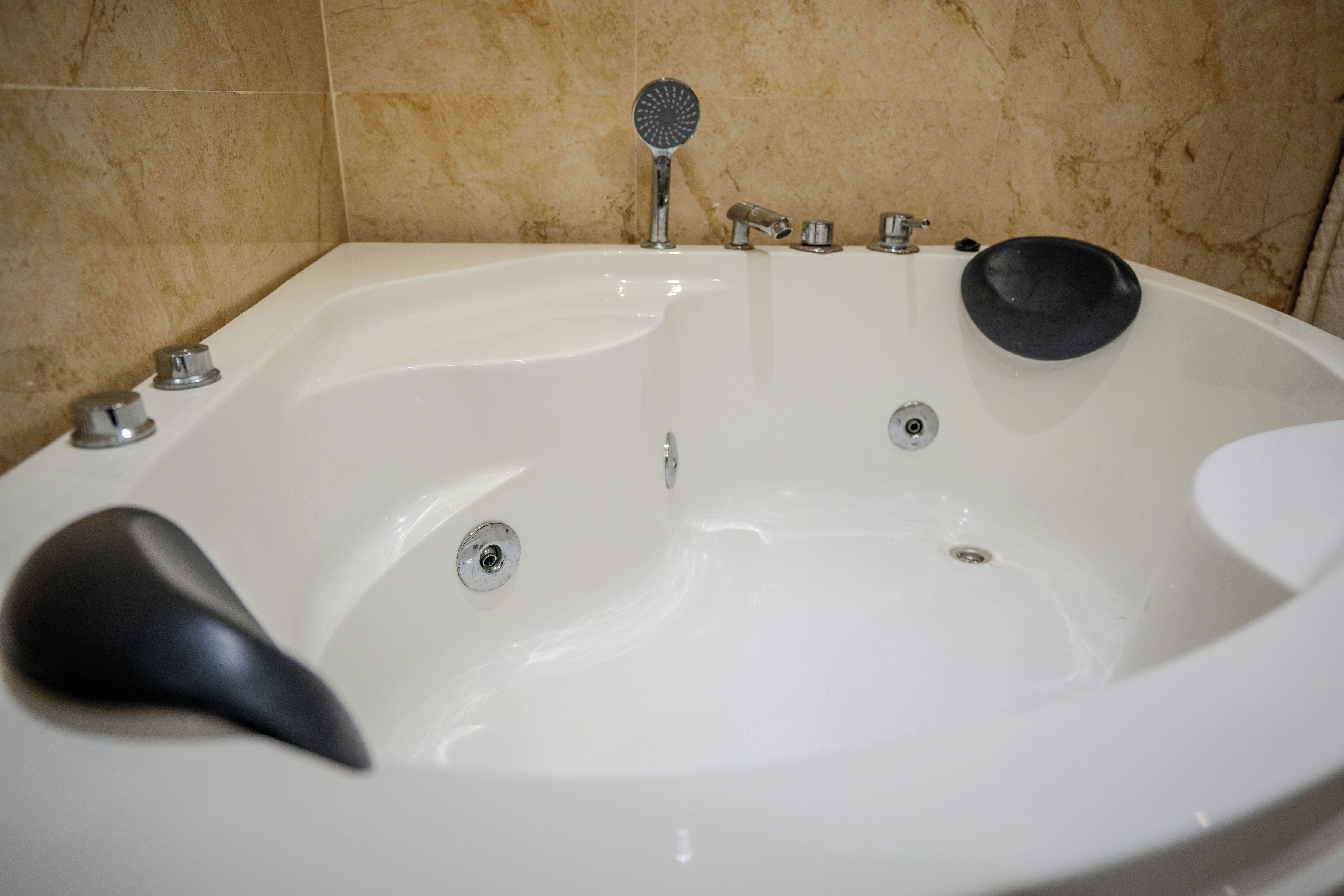 A white bathtub with a black seat, a handheld showerhead, and a black soap dish.